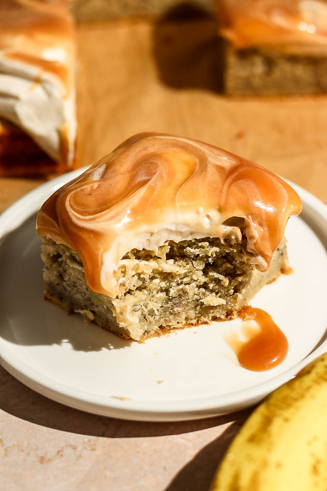 A final close-up view of a bitten slice of caramel banana cake on a white plate, showcasing the rich caramel glaze and soft crumb texture.