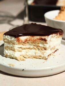 A slice of chocolate eclair cake with a bite missing, set on a white plate.