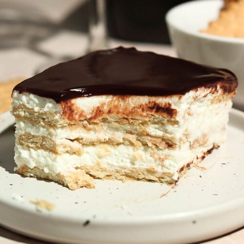 A slice of chocolate eclair cake with a bite missing, set on a white plate.