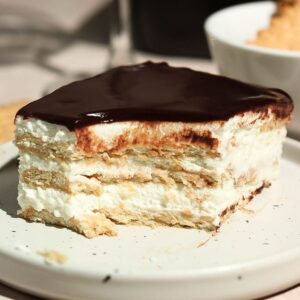 A slice of chocolate eclair cake with a bite missing, set on a white plate.
