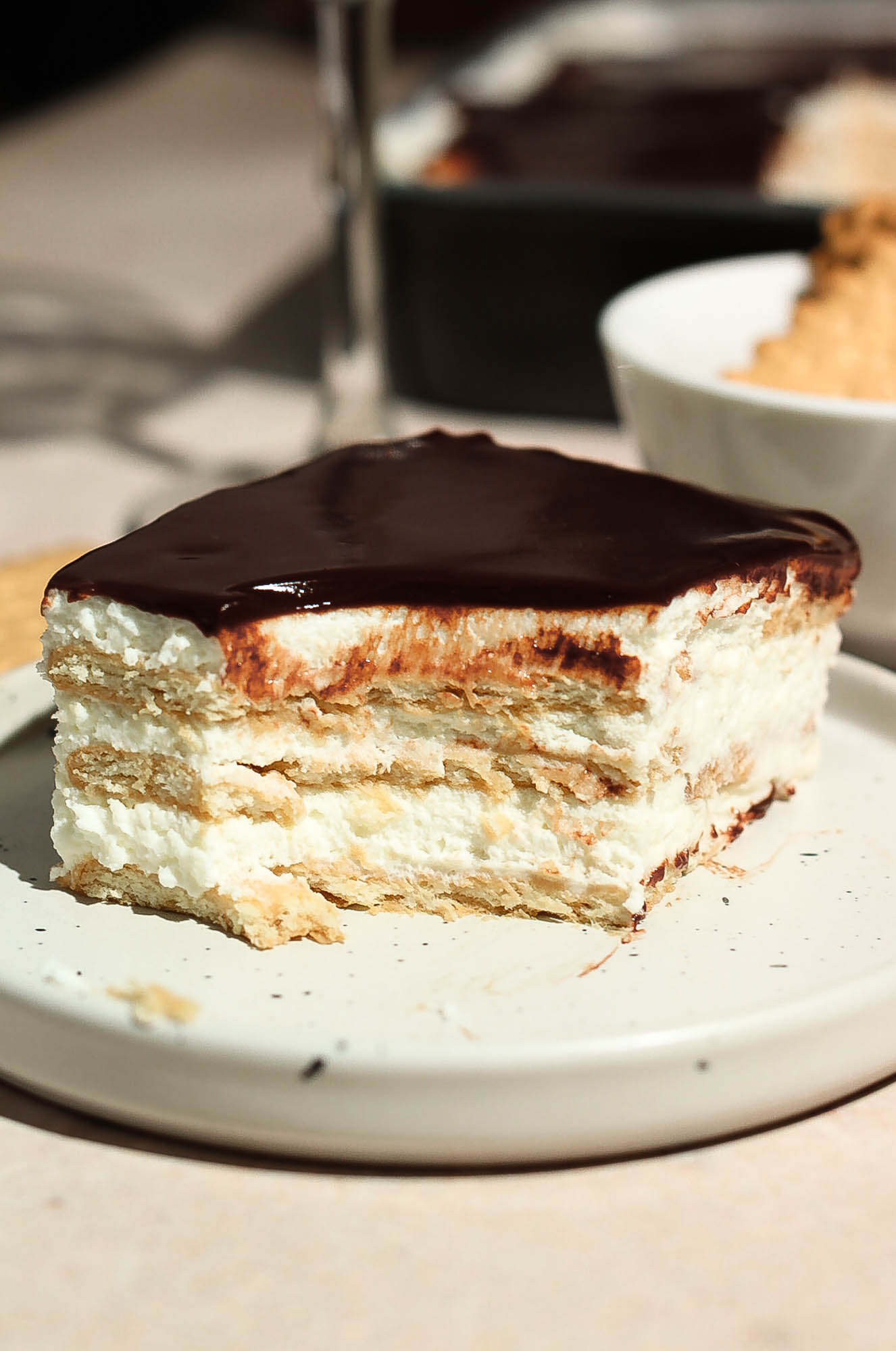 A slice of chocolate eclair cake with a bite missing, set on a white plate.