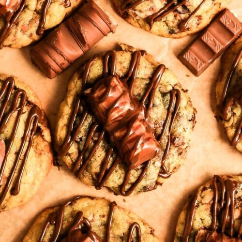 A flat-lay top-down shot of freshly baked Kinder Bueno cookies drizzled with Nutella, with extra candy bars scattered around.