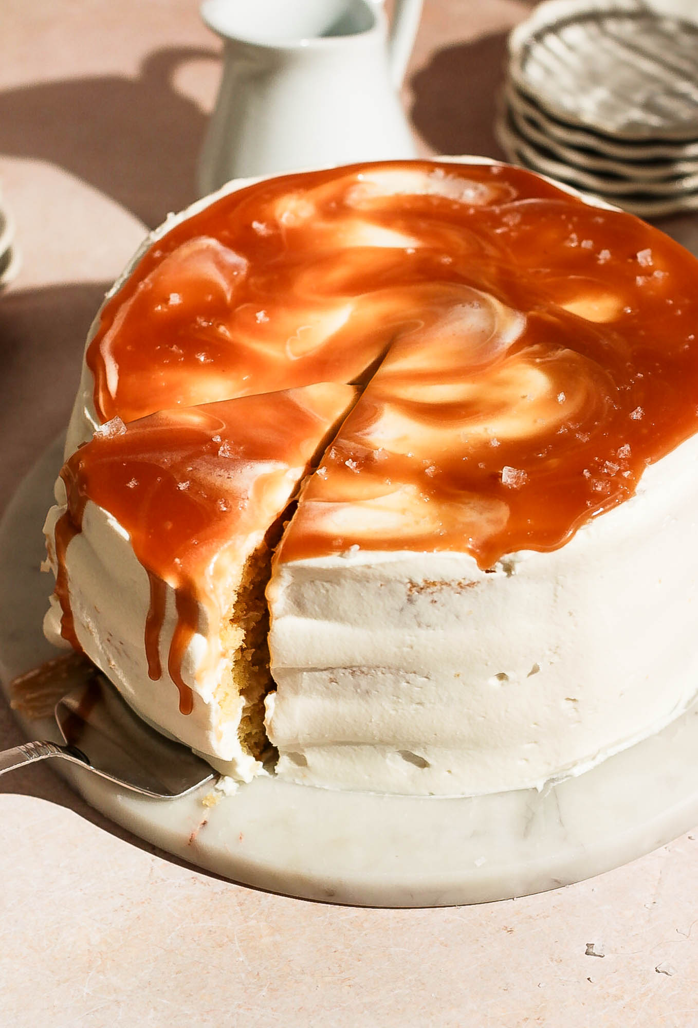 A cake knife cutting a wedge out of a frosted salted caramel layer cake.